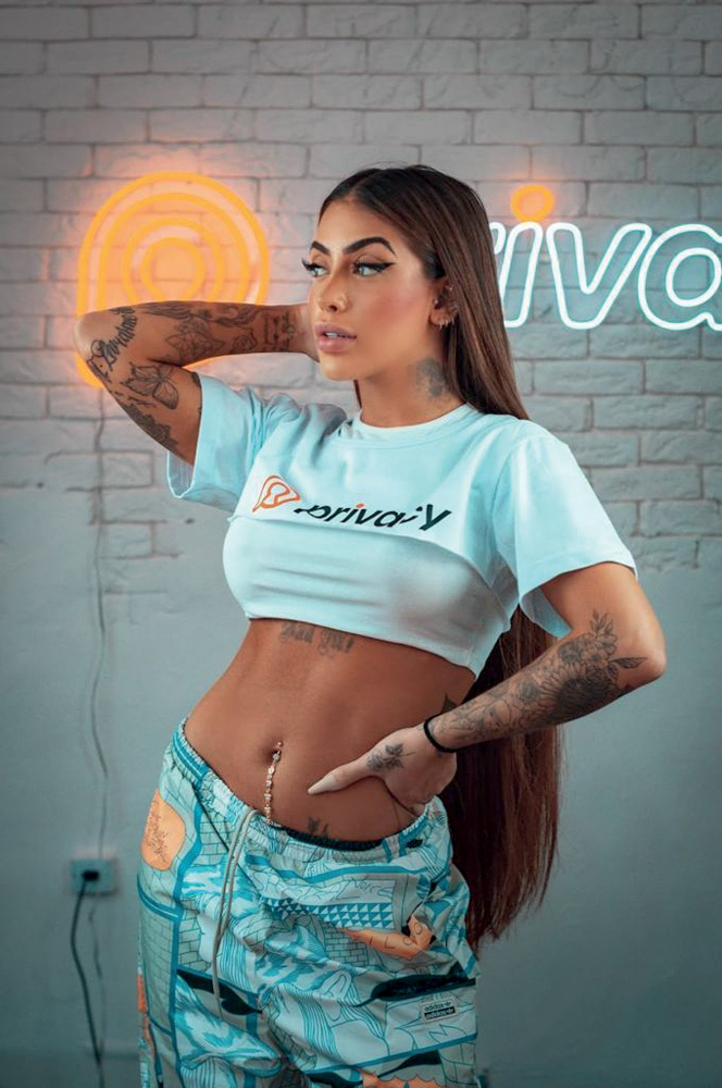 MIRELLA (1).jpeg MC Mirella aparece de saia jeans e cropped azul claro. Ela é uma mulher branca, de pele mais escura, e cabelo preto e liso e comprido.