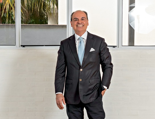 Renato Pacheco Neto, cônsul-geral da Suécia em São Paulo, veste terno escuro com gravata azul-bebê. Sorri para a foto com uma das mãos no bolso e espelhos ao fundo.