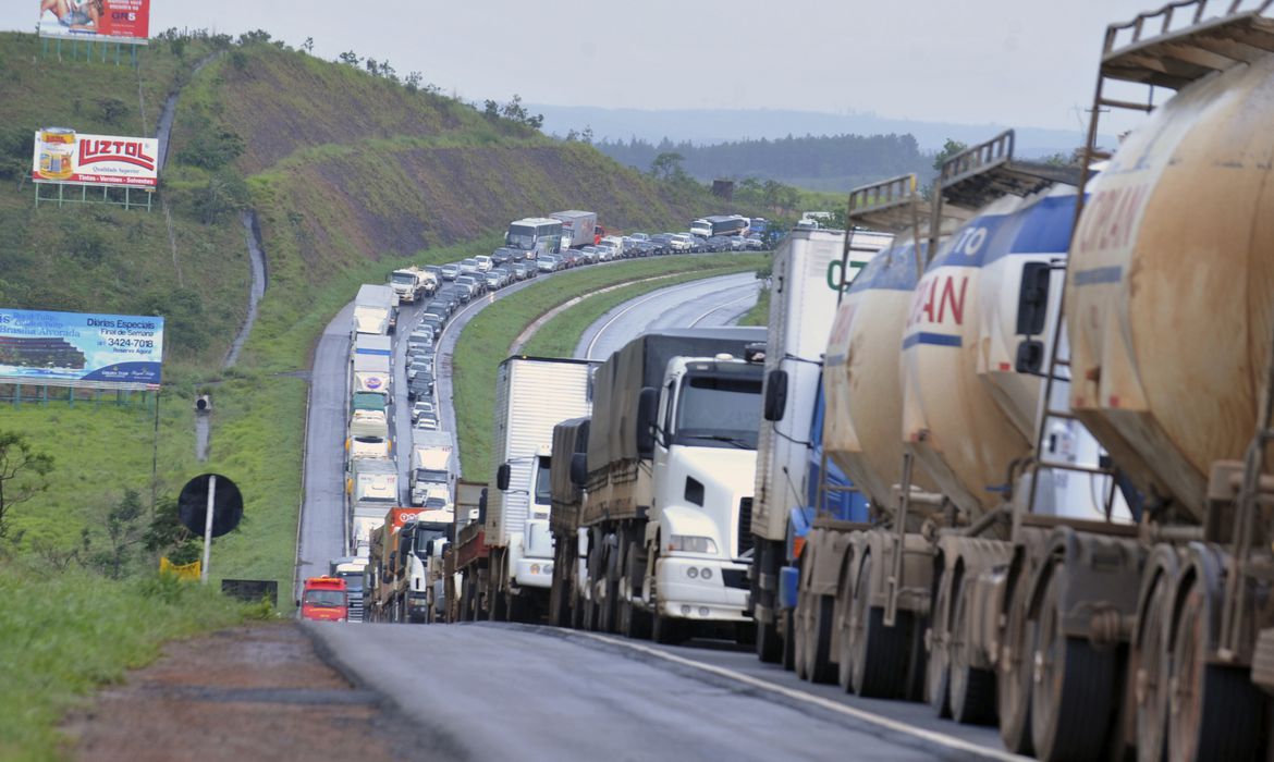 BR-060, que liga Brasília a Goiânia. Foto exibe fila de caminhões em rodovia.
