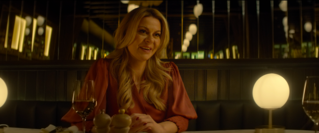 Em um bar, mulher loira, de camisa de cor coral