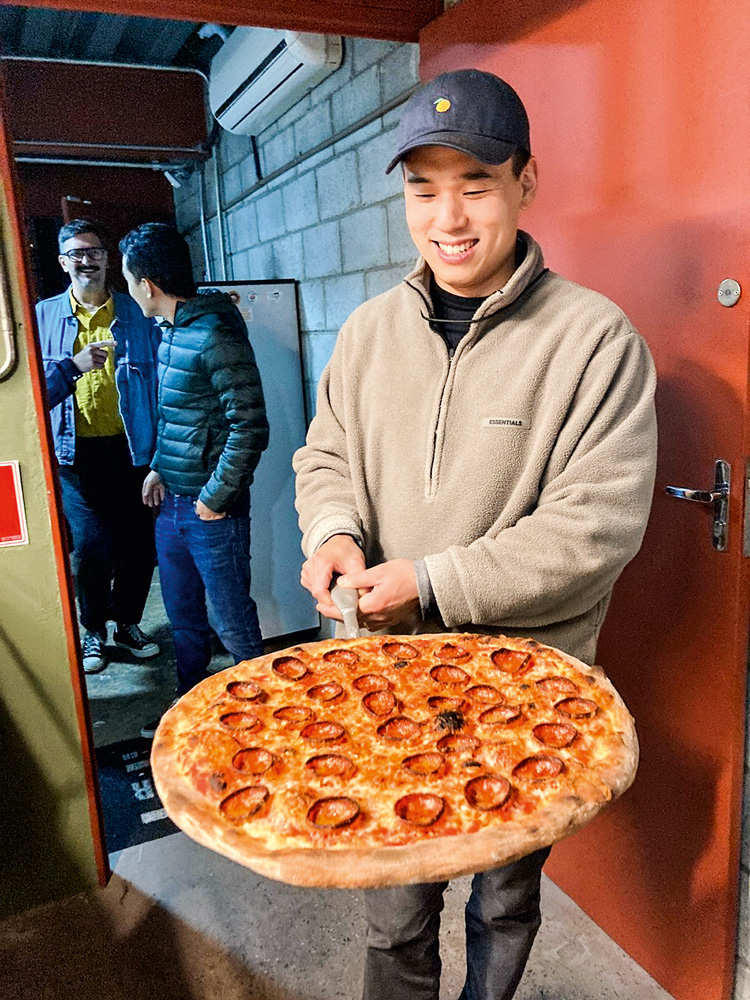 Paul Cho posa segurando um grande disco de pizza