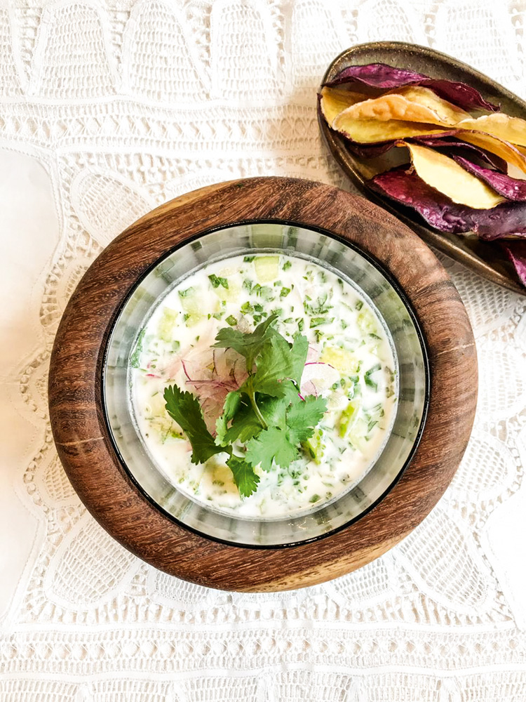 Ceviche decorado por folhas de coentro servido em recipiente de madeira. Ao lado, um recipiente menor, também de madeira, com chips de batata-doce