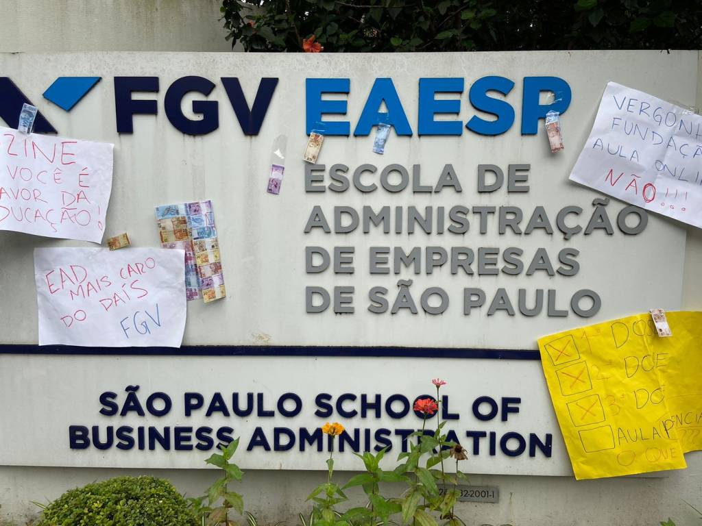 Na imagem, logotipo da FGV EAESP (Escola de administração de empresas de são paulo) na fachada de prédio na Bela Vista. Cartazes com frases de protesto, pedindo volta das aulas presenciais, foram colados junto do nome da faculdade