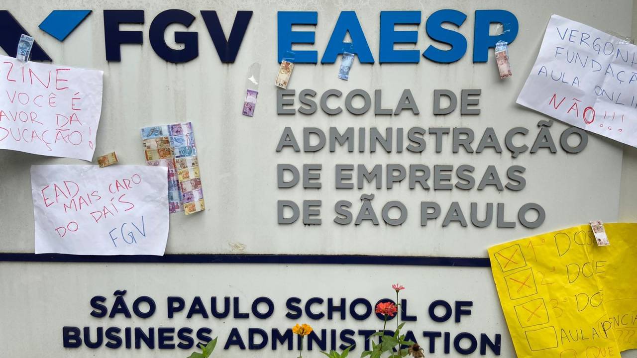 Na imagem, logotipo da FGV EAESP (Escola de administração de empresas de são paulo) na fachada de prédio na Bela Vista. Cartazes com frases de protesto, pedindo volta das aulas presenciais, foram colados junto do nome da faculdade
