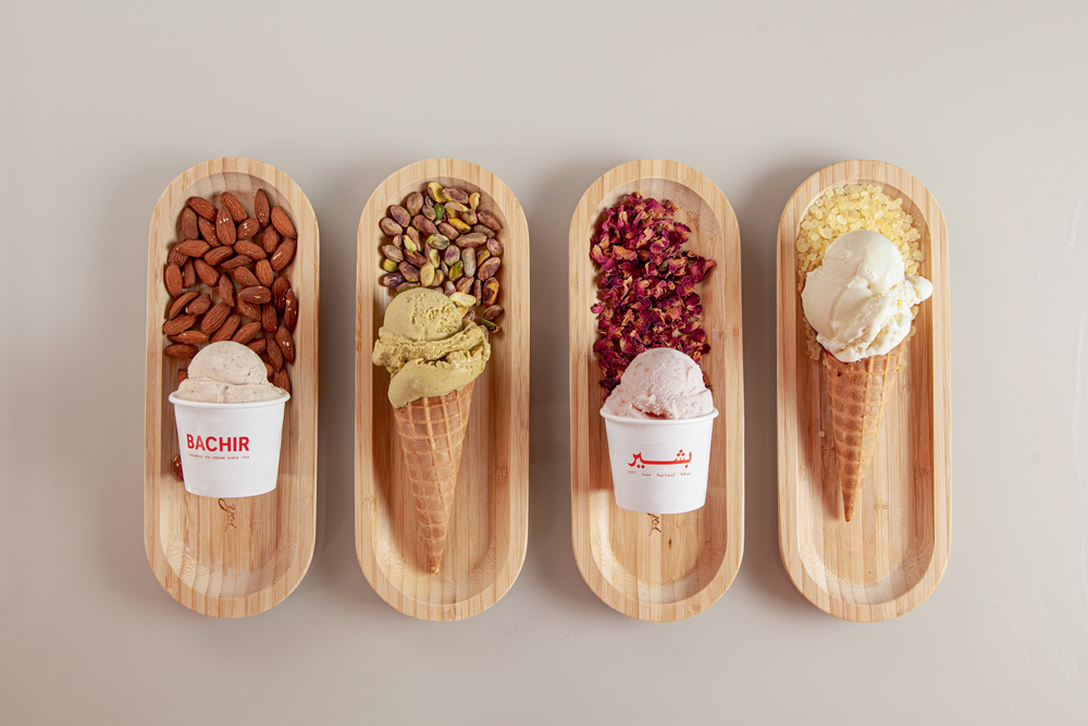 Quatro cones de diferentes sabores de sorvetes estão dispostos sobre pequenas tábuas de madeira sobre uma mesa