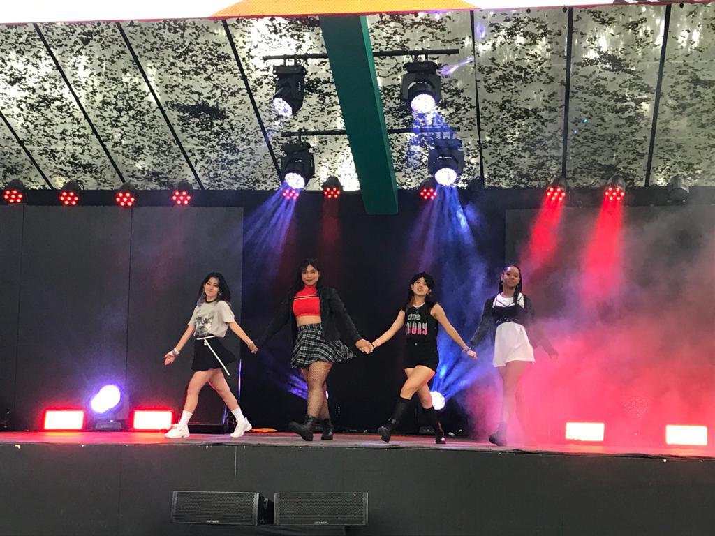 k pop Foto mostra quatro adolescentes no palco, três brancas e uma negra. Elas usam roupas similares às roupas dos ídolos de bandas de K-Pop.