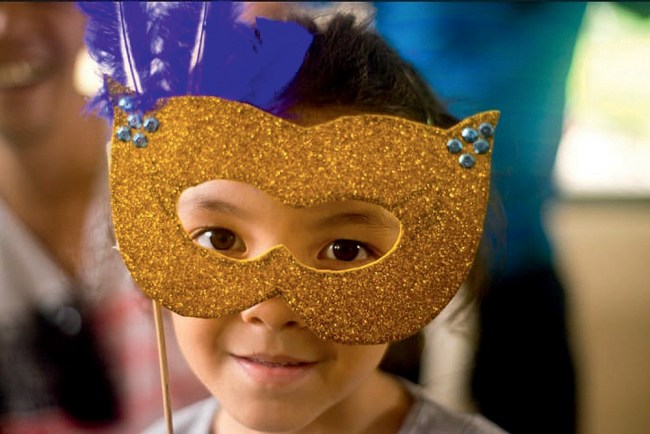Uma menina segura uma máscara dourada de carnaval em frente ao rosto