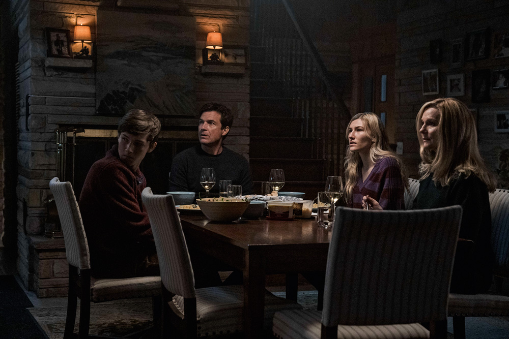 Imagem mostra mesa de jantar com 4 pessoas sentadas, dois homens e duas mulheres. A sala é escura.
