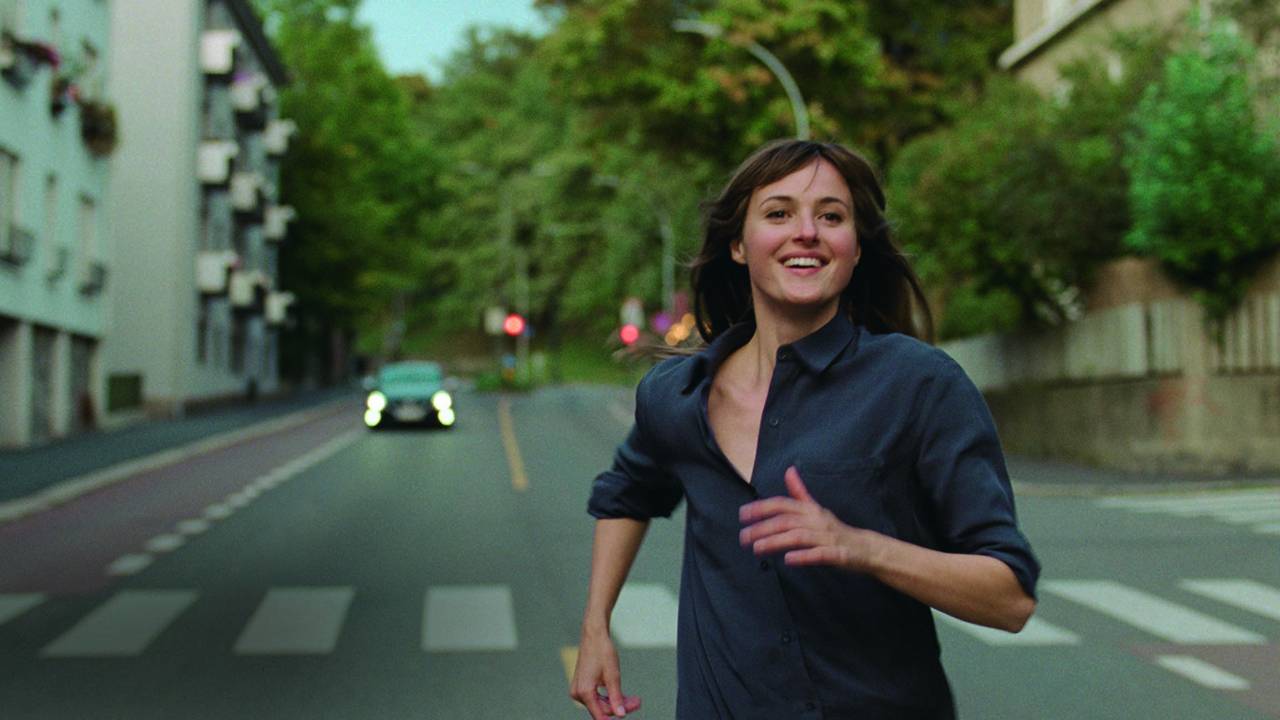 Imagem mostra mulher correndo sorrindo em rua.