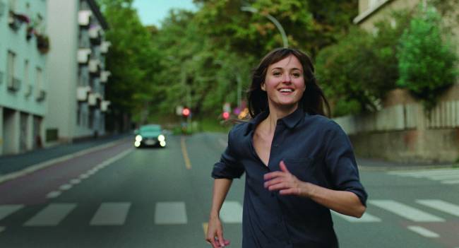 Imagem mostra mulher correndo sorrindo em rua.