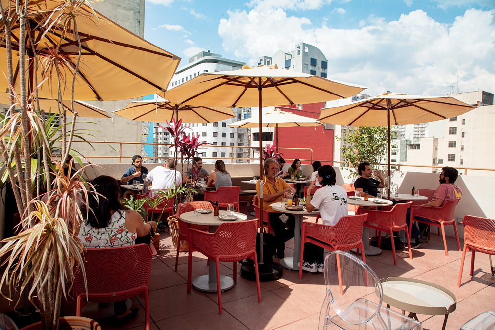 Ambiente ao ar livre do restaurante Cora decorado por cadeiras de cor avermelhada, guarda-sóis e mesas