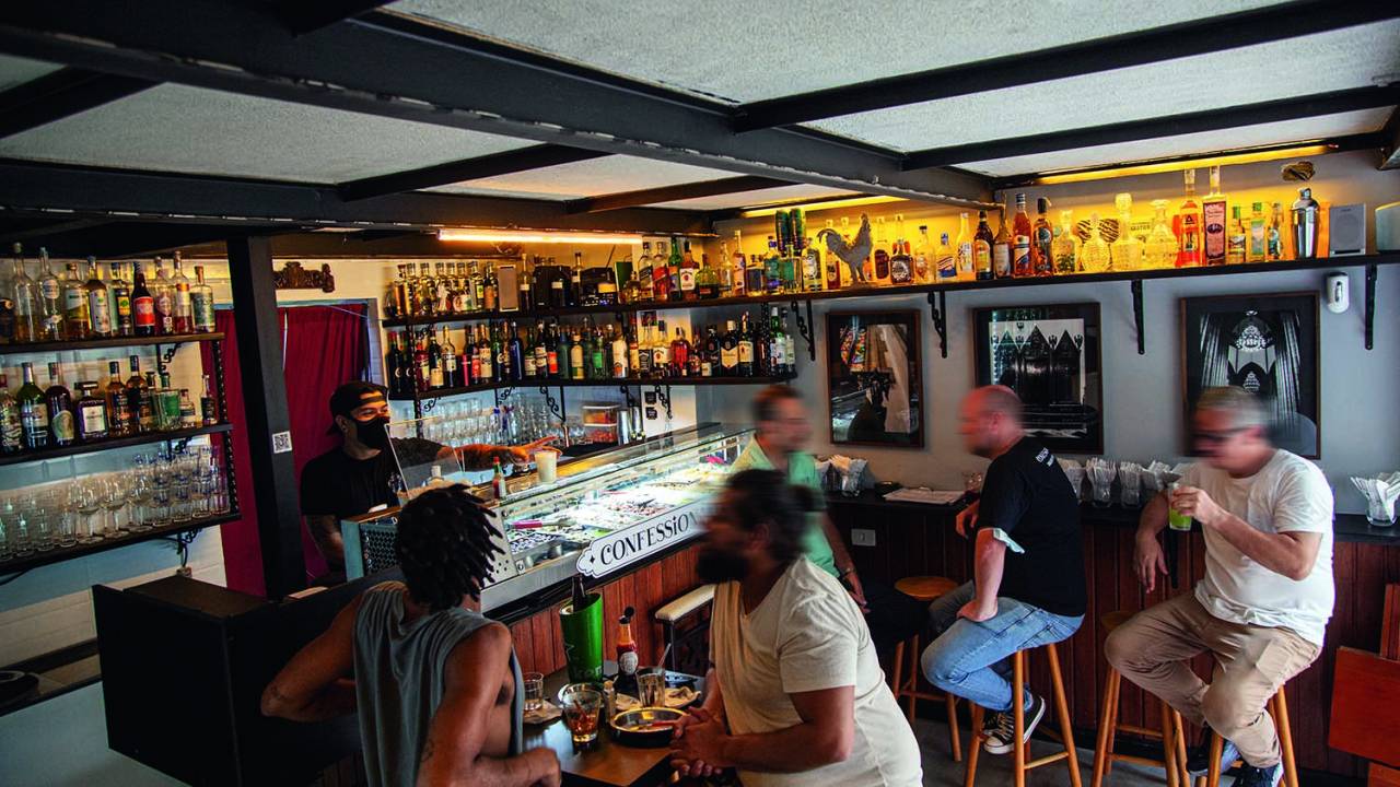 Ambiente do bar Confessionário decorado por garrafas, fotos na parede e uma vitrine no balcão