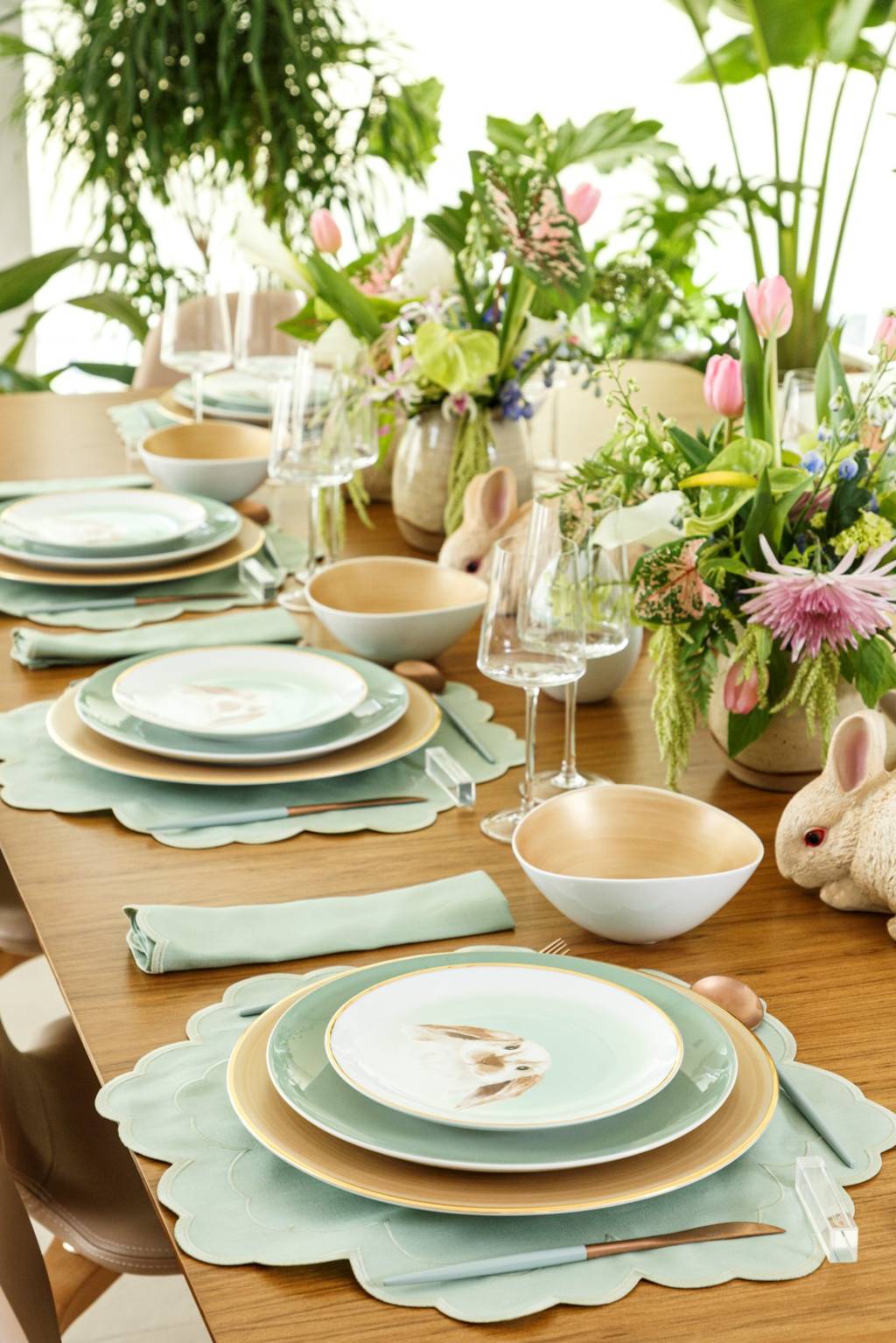 Mesa com temática de Páscoa exibe pratos com coelho no centro e plantas na mesa.
