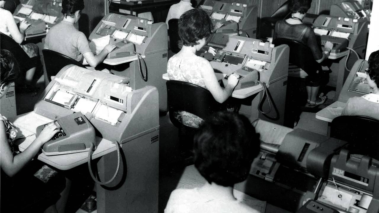 Imagem em preto e branco mostra diversas mulheres sentadas em escrivaninhas trabalhando em máquinas de escrever