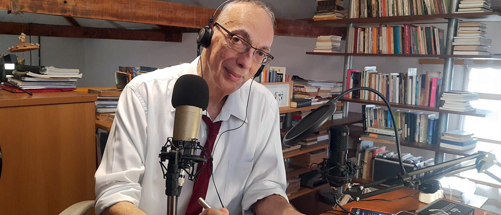 Fabio Malavoglia.jpg Imagem mostra homem careca de terno em mesa com fone e microfone.