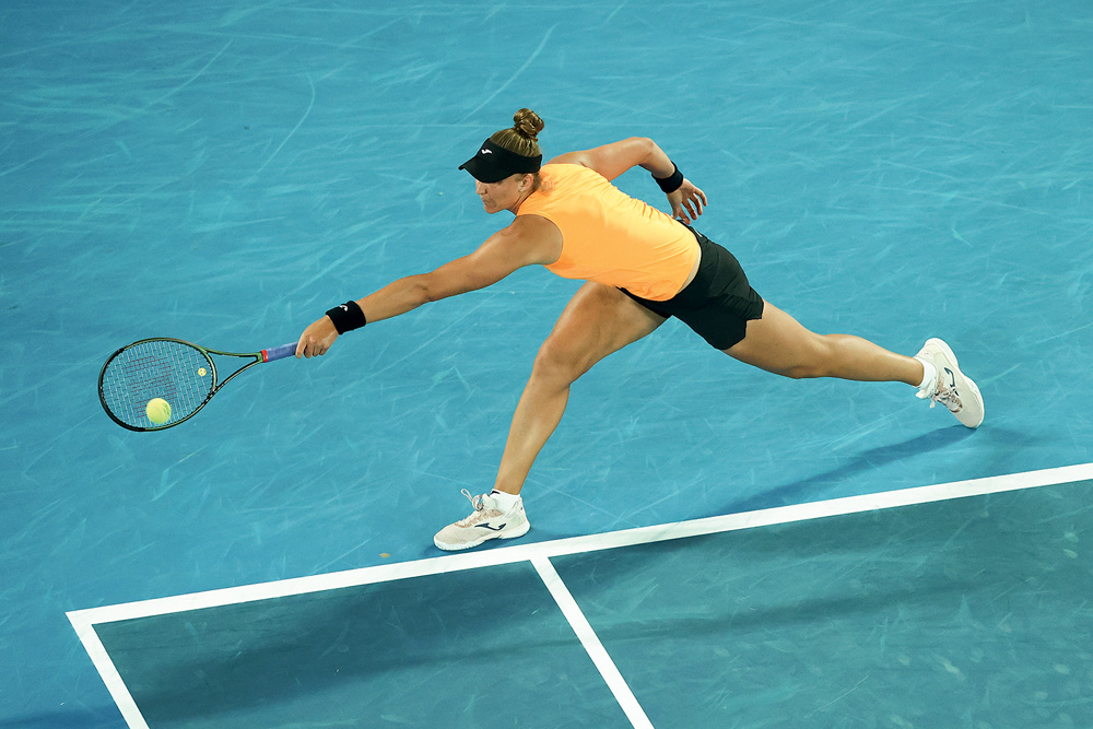 Bia joga em uma quadra de tênis, ela segura a raquete e veste uma roupa específica para o esporte. Seu cabelo loiro está preso em um coque
