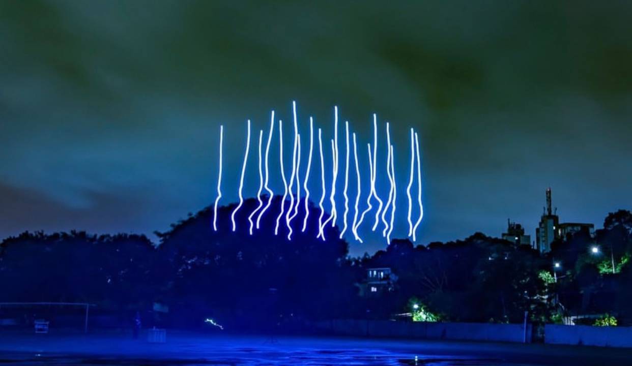 Imagem mostra projeção de luzes em formato de linhas rabiscadas azuis no céu.