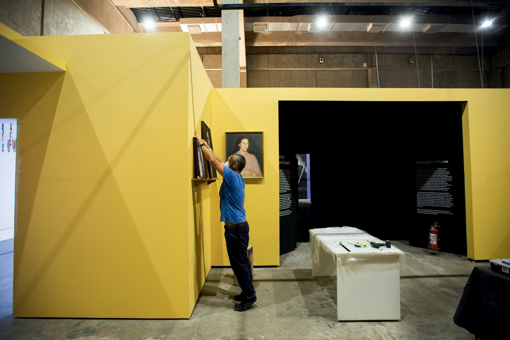 Imagem mostra homem pendurando cartaz em parede amarela.