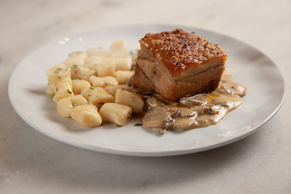 Pancetta assada servida junto de nhoque e cogumelos em prato raso de cor branca