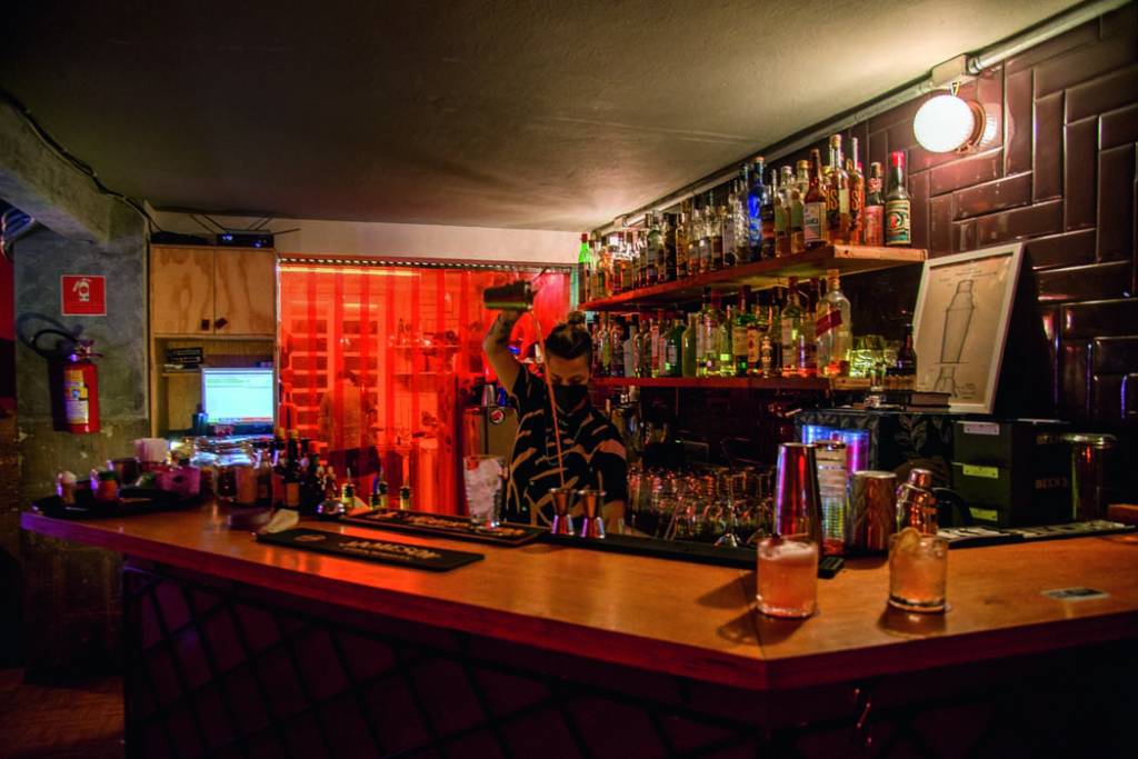 Imagem mostra balcão de bar com bartender fazendo um drink.