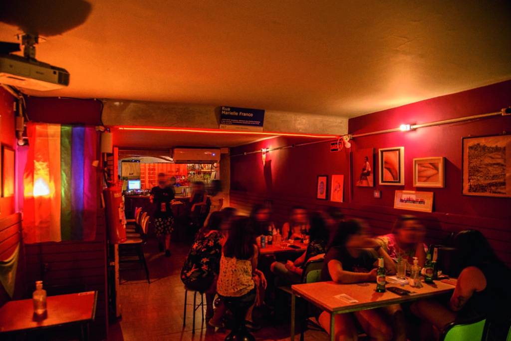 Imagem mostra interior de bar com luzes vermelhas e paredes coloridas.