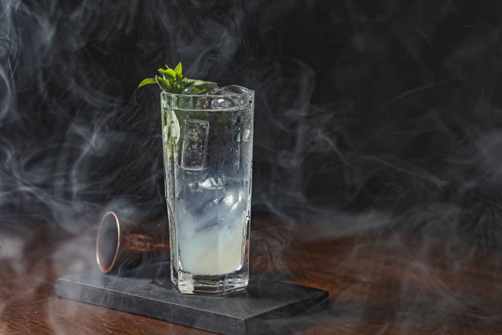 Drinque servido em copo longo envolto em fumaça
