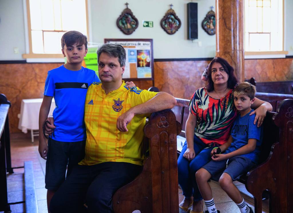 Imagem mostra família - um casal e dois filhos - sentados em bancos de igreja.
