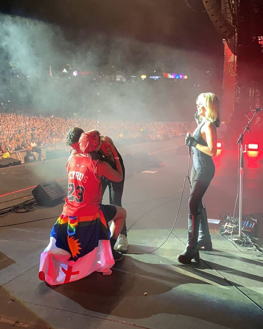 Vinicius Lasserre e Victor Delmas (REPRODUÇÃO-INSTAGRAM) Foto mostra Miley Cyrus de pé no palco enquanto casal se abraça durante pedido de casamento, com plateia de fundo. Vinicius veste regata vermelha e tem a bandeira de Pernambuco amarrada na cintura.