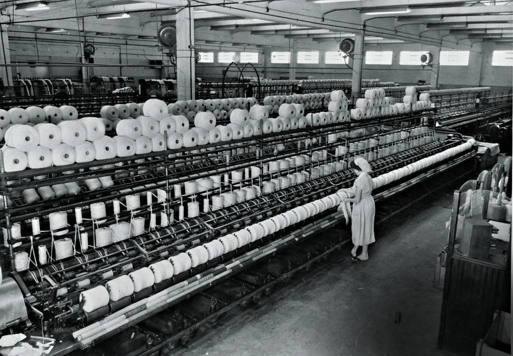 Imagem mostra mulher trabalhando em linha com diversos rolos de lã.