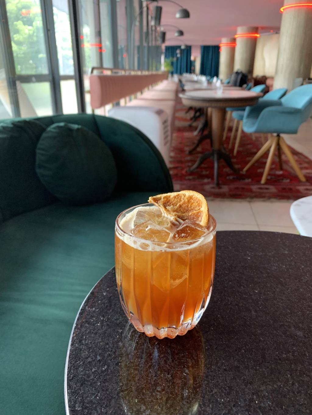 Foto de drinque de cor alaranjada servido em copo baixo decorado por um pedaço de laranja desidratada