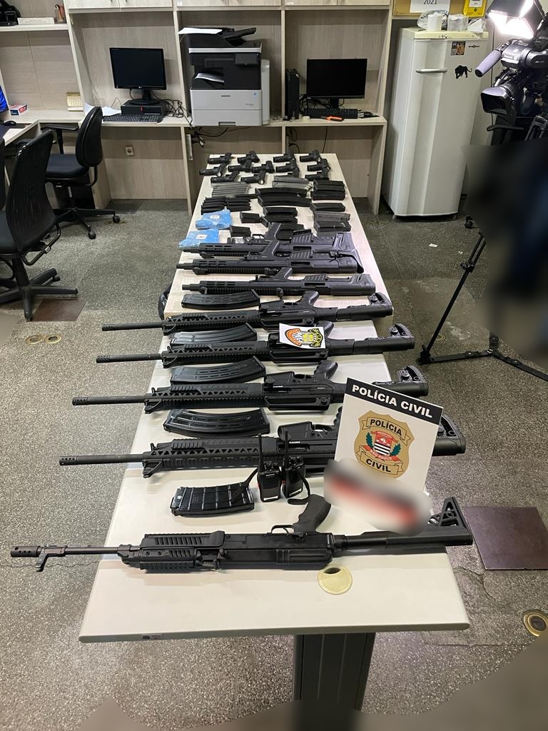 Imagem mostra dezenas de fuzis e pistolas dispostos em mesa de delegacia
