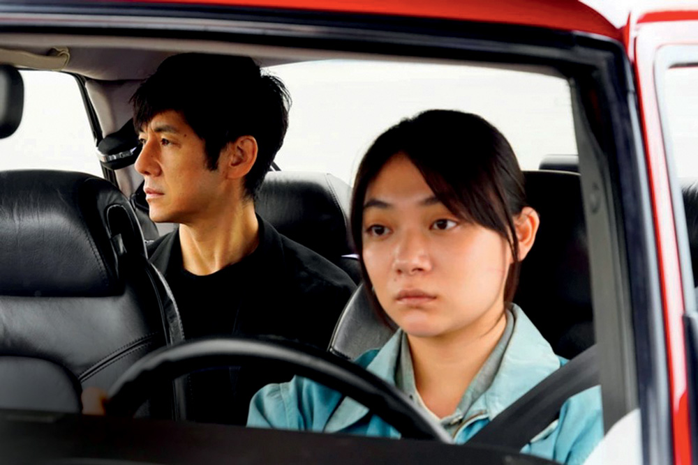 Imagem mostra mulher dirigindo carro com homem no banco de trás.