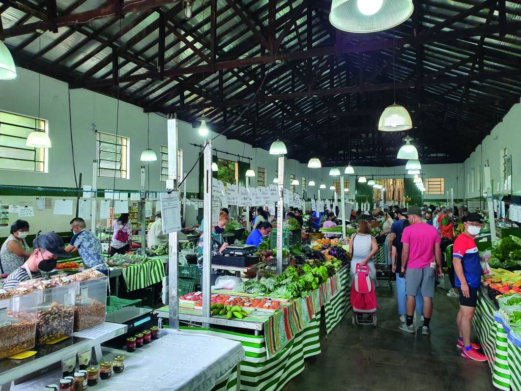 feira.jpg Imagem mostra espaço com diversos balcões com vegetais e frutas.