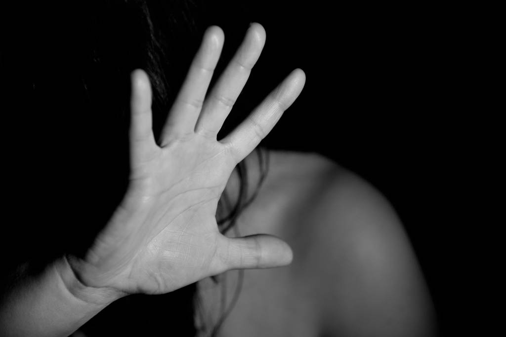 Imagem mostra mulher com mão levantada em ambiente escuro