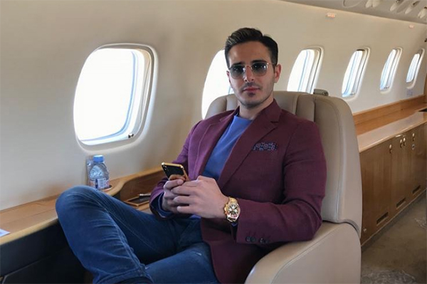Imagem mostra Simon, usando blazer, sentado em poltrona de jatinho de luxo