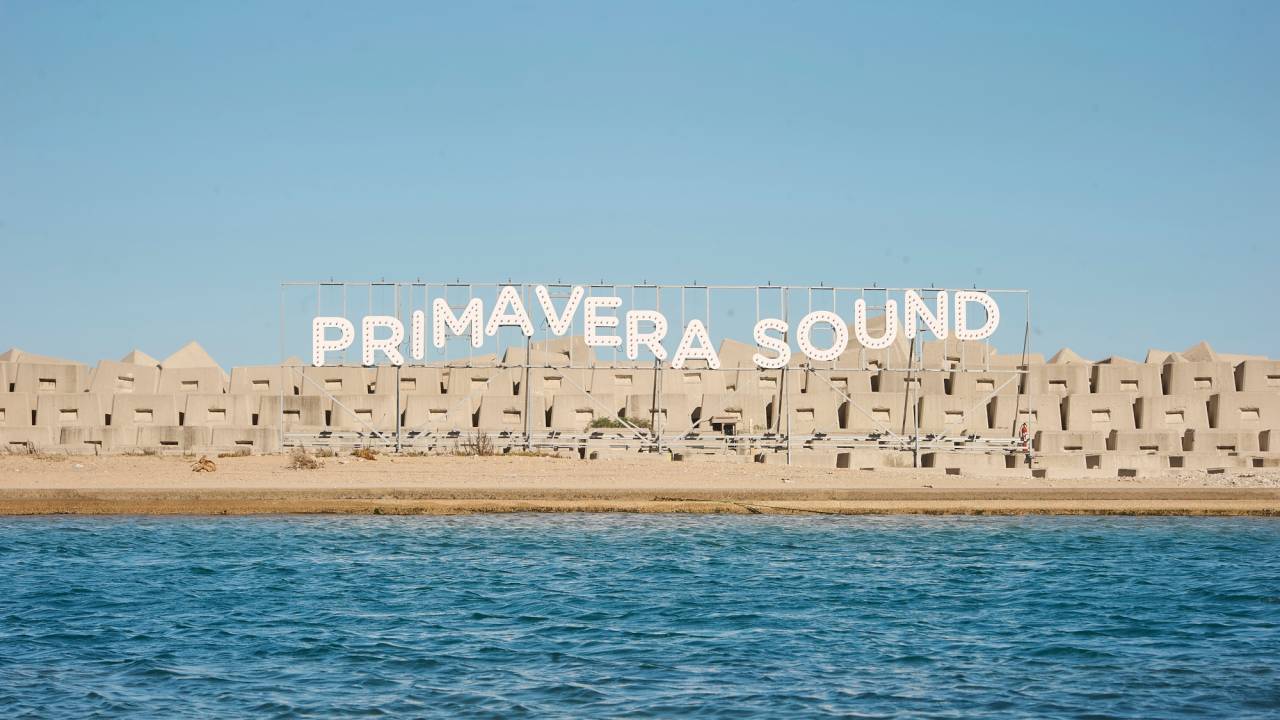 Imagem mostra outdoor escrito "Primavera Sound", em letras brancas, sobre pedras, no mar.