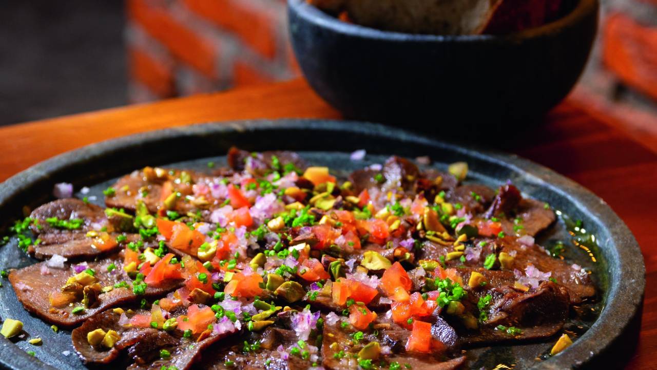 Língua de boi servida em panelinha junto de pedaços de tomate e outros