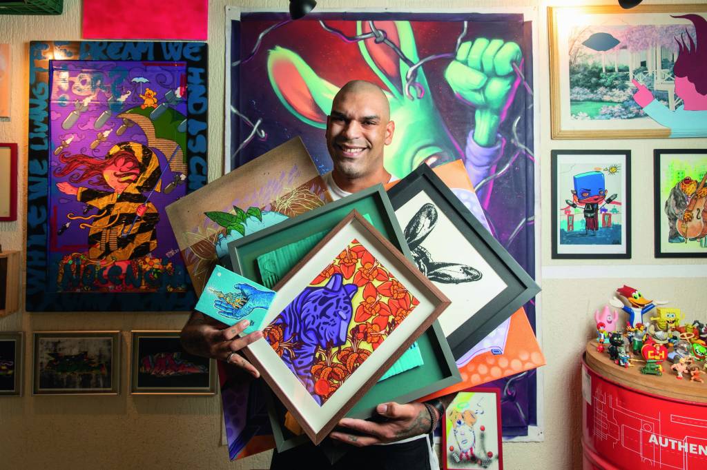 COLECIONADORES DE ARTE Imagem mostra homem careca segurando diversos quadros de graffitti.