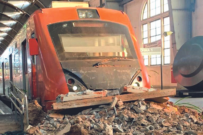 Imagem mostra trem com pintura vermelha e escombros na sua frente.