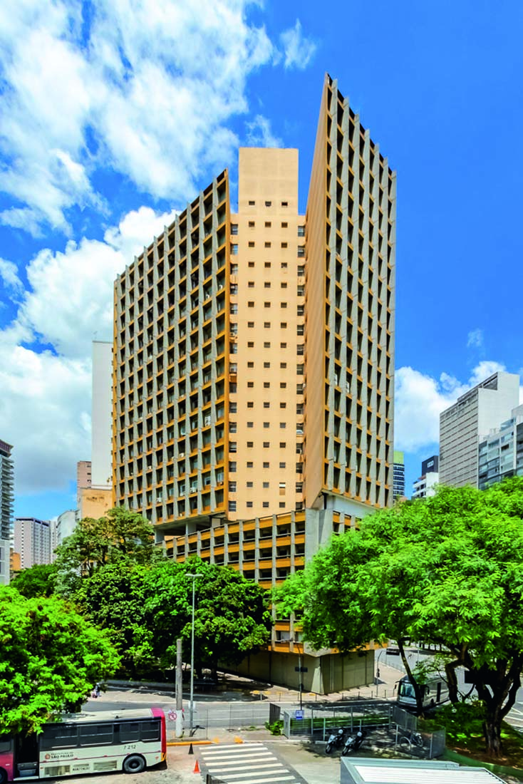 Foto mostra o Edifício Praça da Bandeira. O seu está claro, com poucas nuvens. É possível ver as árvores em volta do prédio