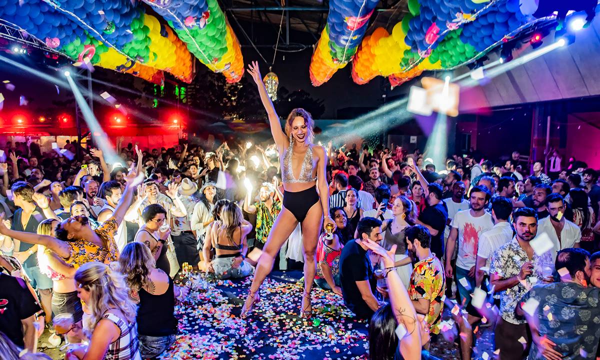 Pessoas em uma festa com uma mulhe rno centro e balões coloritos no teto