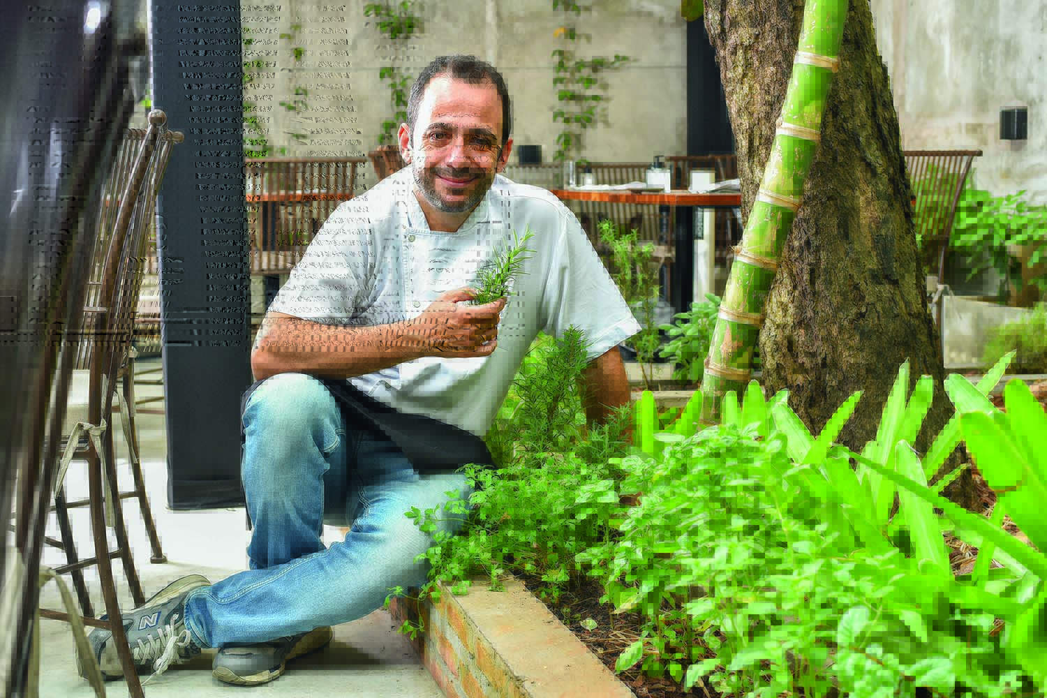 Chef posa ao lado de uma pequena horta cultivada no ambiente externo do restaurante