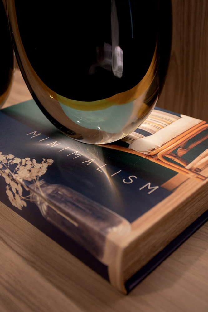 Detalhes do apartamento luxuoso da maternidade: um livro de capa dura e um vaso brilhante em cima de uma das mesas