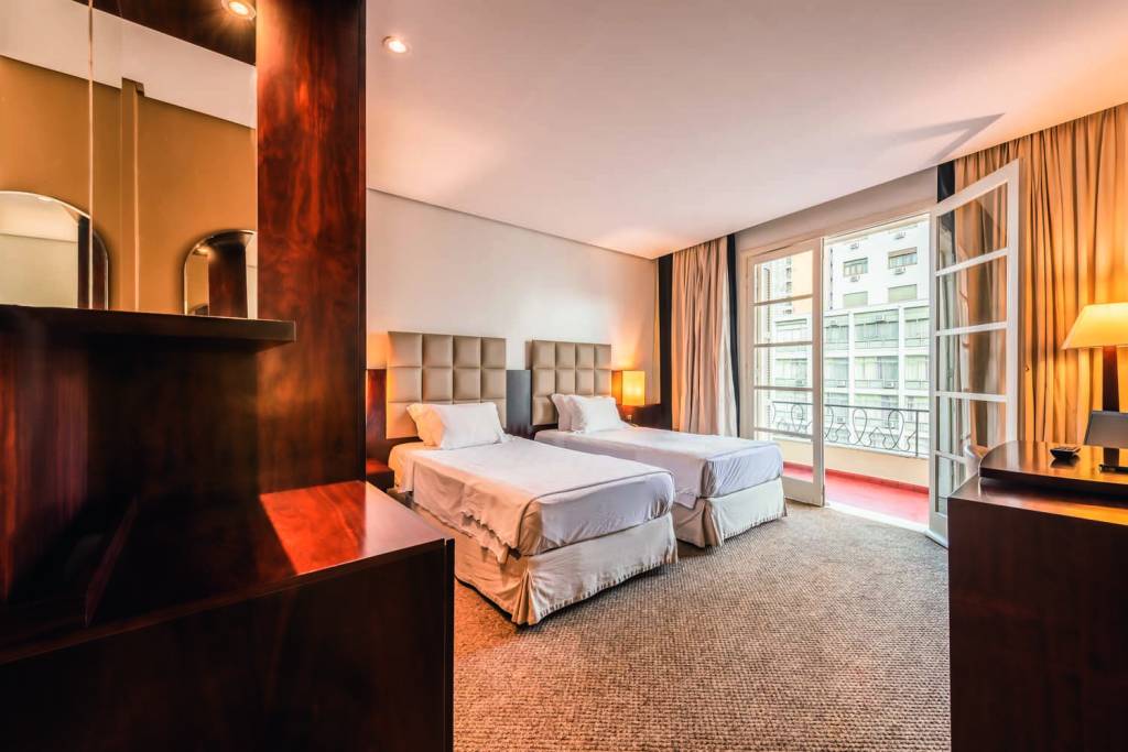 Imagem mostra quarto de hotel com duas camas e varanda