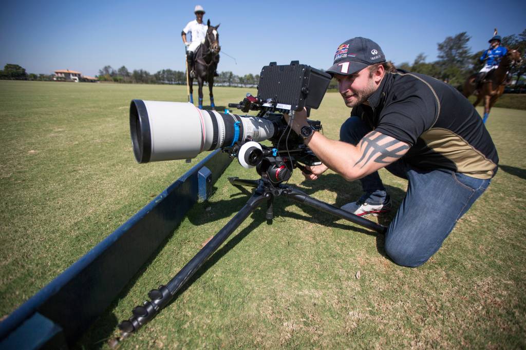 Raphael Macek, fotógrafo especializado em cavalos, posa de joelhos com câmera instalada em gramado.