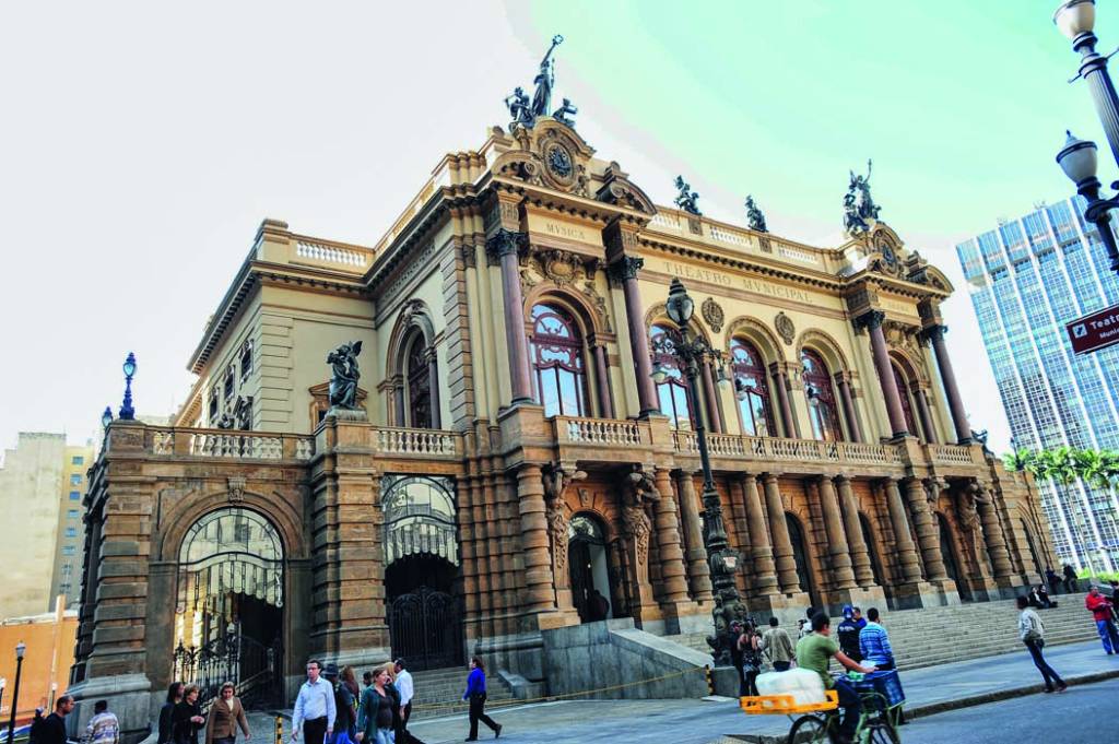 Teatro Municipal em São Paulo visto em sua extensão. Pessoas andam na rua que está na frente