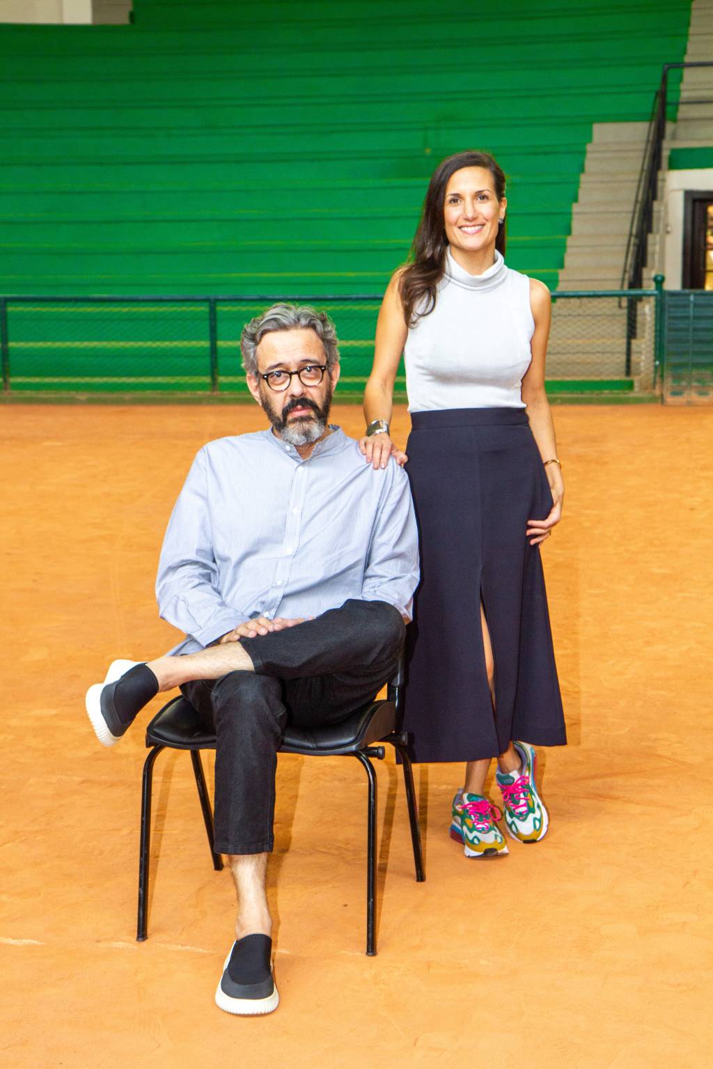 Waldick Jatobá e Camilla Barella, das feiras Made e ArPa, posam em um grande estádio com chão cor de areia. Ele está sentado de pernas cruzadas e ela de pé ao lado, com saia preta e blusa sem mangas branca.