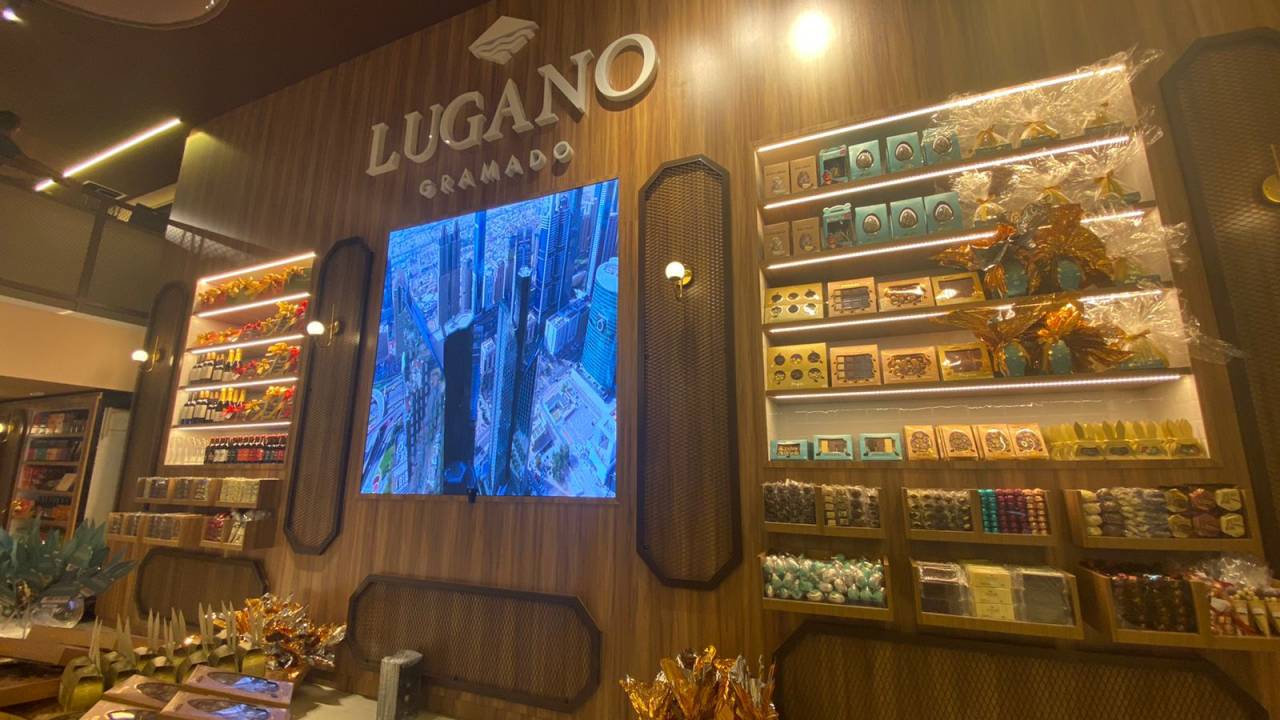foto dupla: imagem de um tablete de chocolate oval da marca Lugano e a fachada da nova loja sendo arrumada por um funcionário