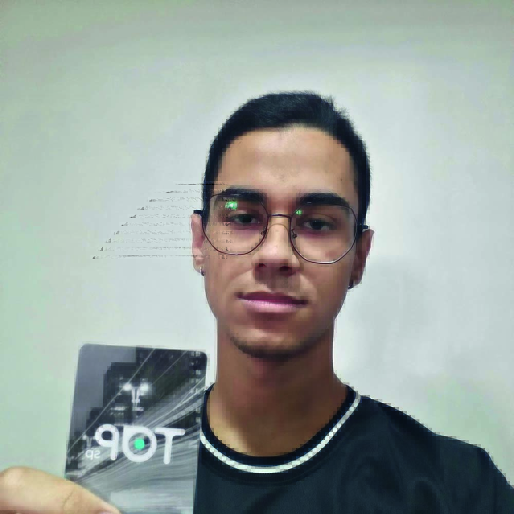 João Vitor Sousa aparece de óculos e camiseta preta segurando seu cartão TOP com a mão
