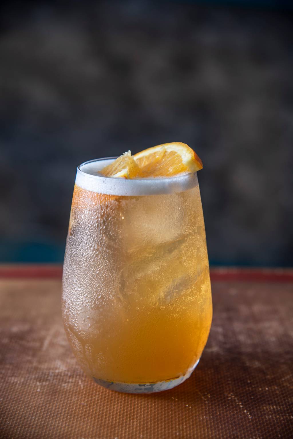 Drinque de cor levemente alaranjada servido em copo baixo decorado por fatias de laranja